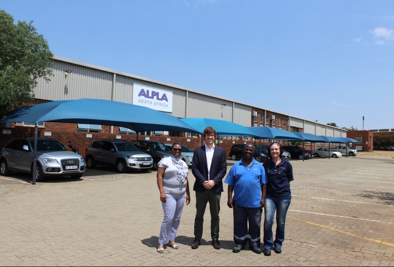 A group of ALPLA employees standing in front of the ALPLA production facility in Kempton Park, South Africa, during the foundation of the AMET Region in 2014, with the ALPLA logo visible on the building